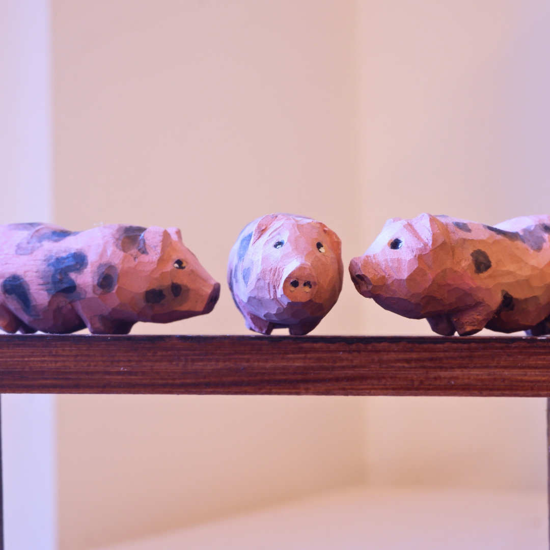 Three hand-carved wooden piglet figurines with spotted markings displayed on a shelf, anornament Snuggle Pigs set