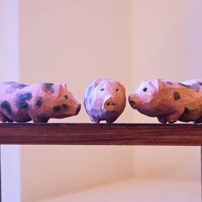 Three hand-carved wooden piglet figurines with spotted markings displayed on a shelf, anornament Snuggle Pigs set